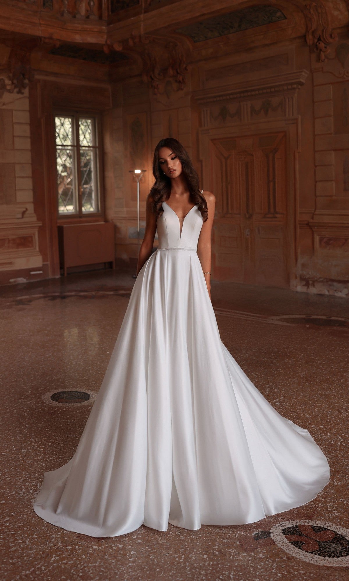 A woman wearing the Alyce 7024 Long Formal Dress, featuring a white A-line skirt, stands in an ornate historic room with wood-paneled walls and large windows.